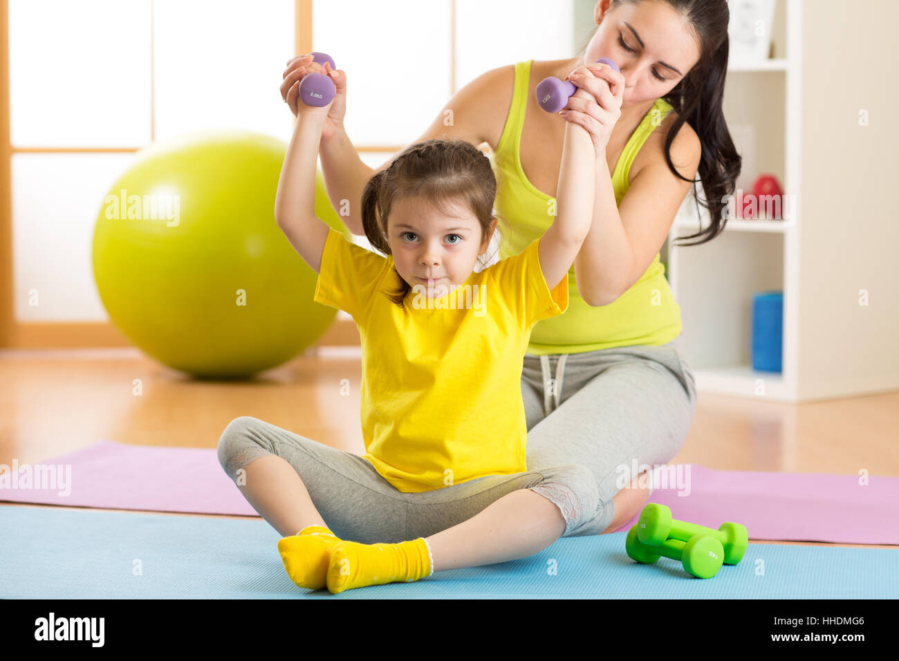 Woman helps little child doing fitness exercises with dumbbells in gym