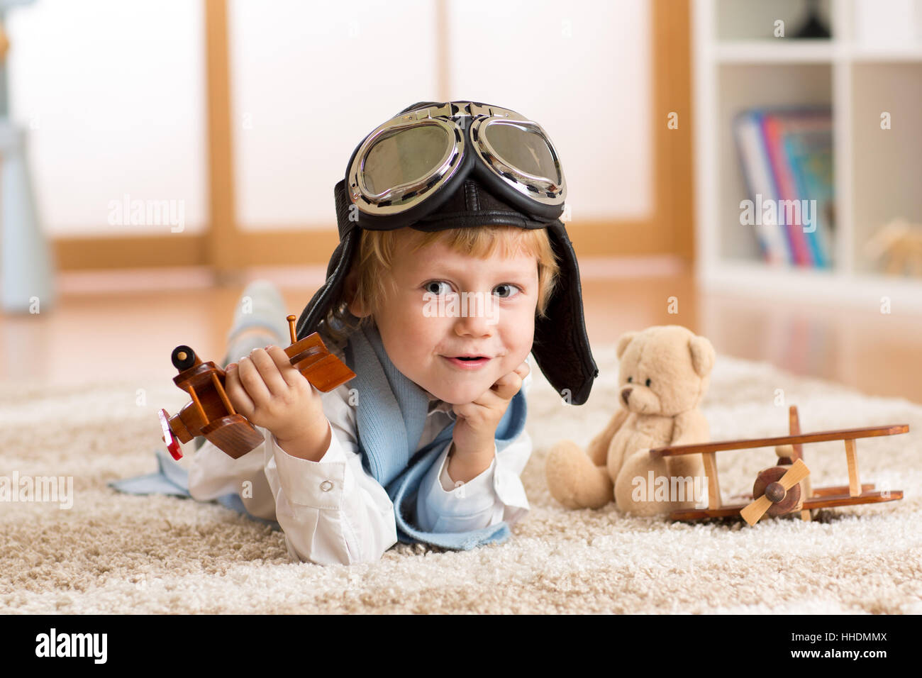 Concept of dreams and travels. Child weared pilot or aviator plays with a toy airplane at home in nursery room Stock Photo