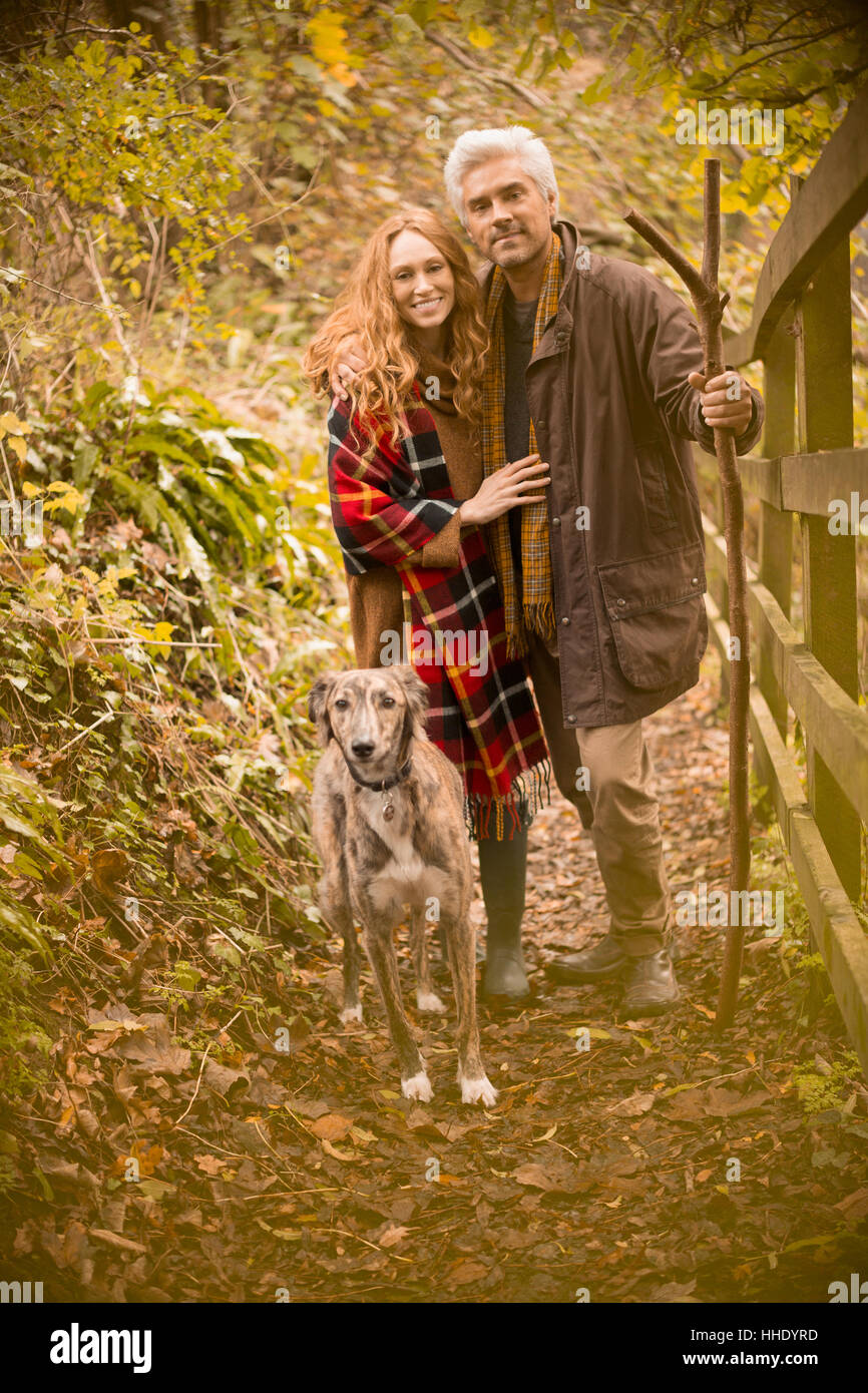 Portrait smiling couple with dog and walking stick along autumn fence Stock Photo
