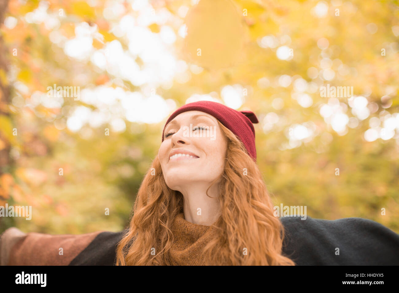 Carefree woman standing under autumn trees with arms outstretched Stock Photo