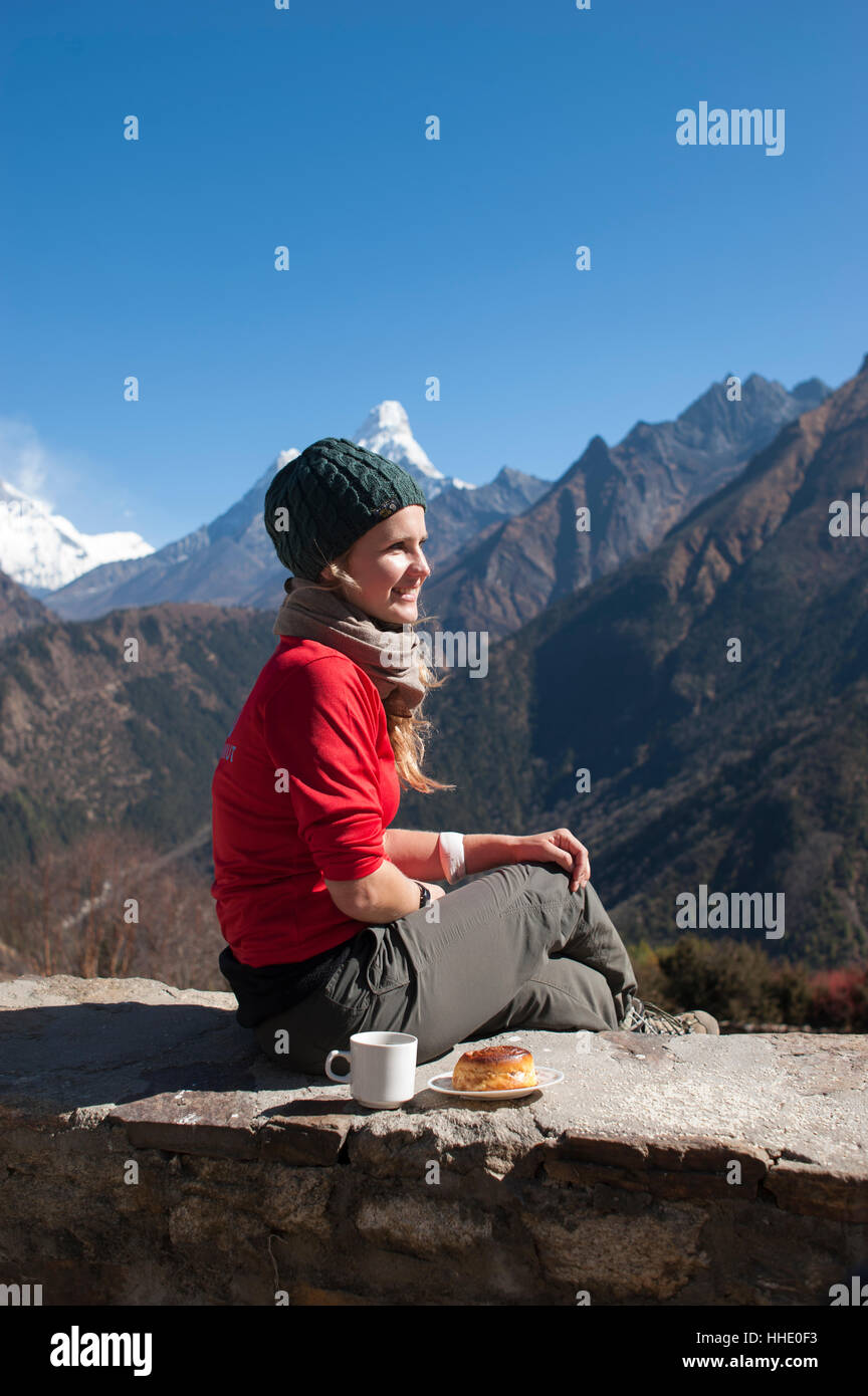 A trekker stops on the trail for some fuel, with Ama Dablam is the peak visible in the distance, Khumbu Region, Nepal Stock Photo