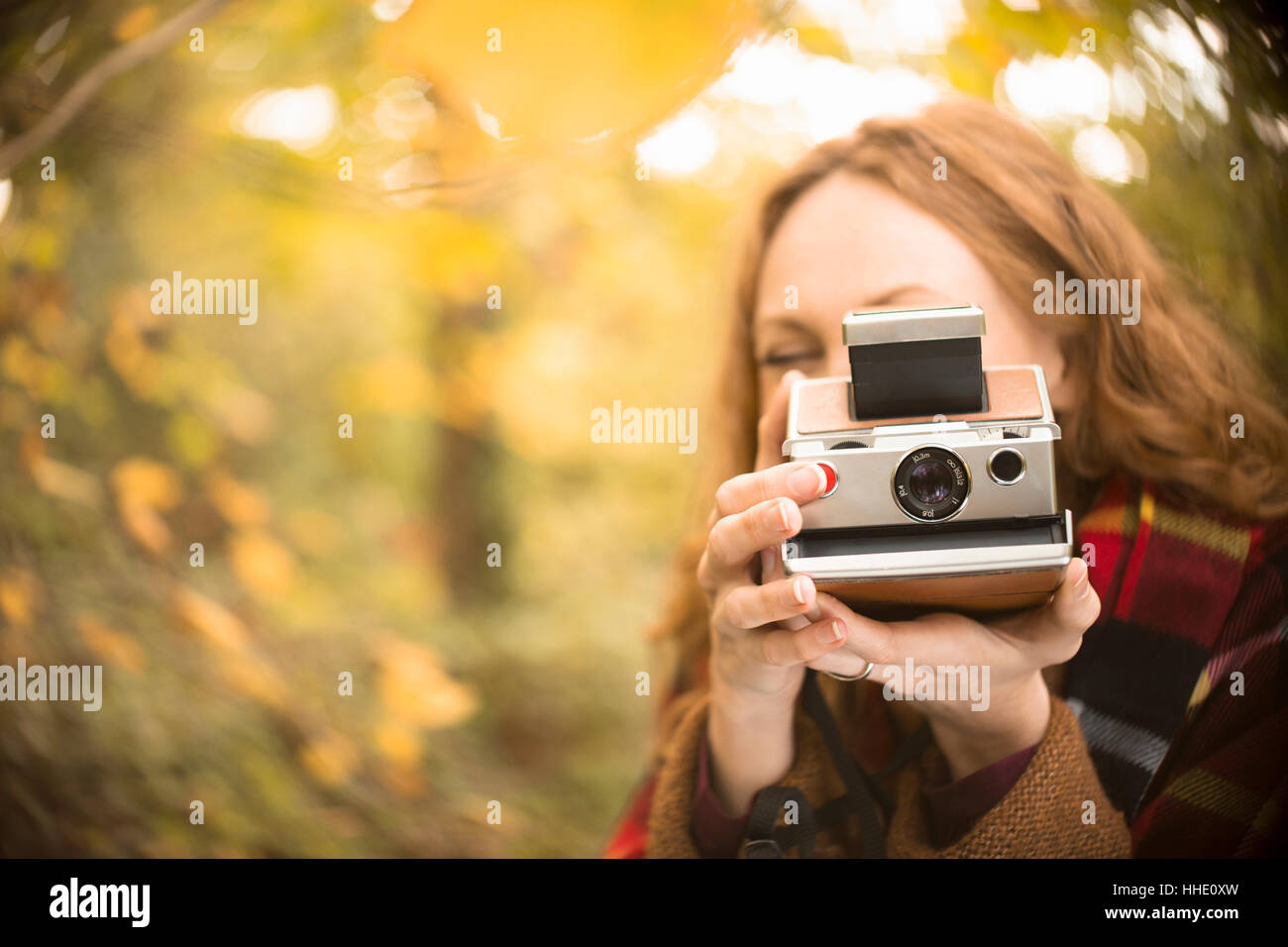 Portrait woman using old-fashioned instant camera in autumn woods Stock Photo