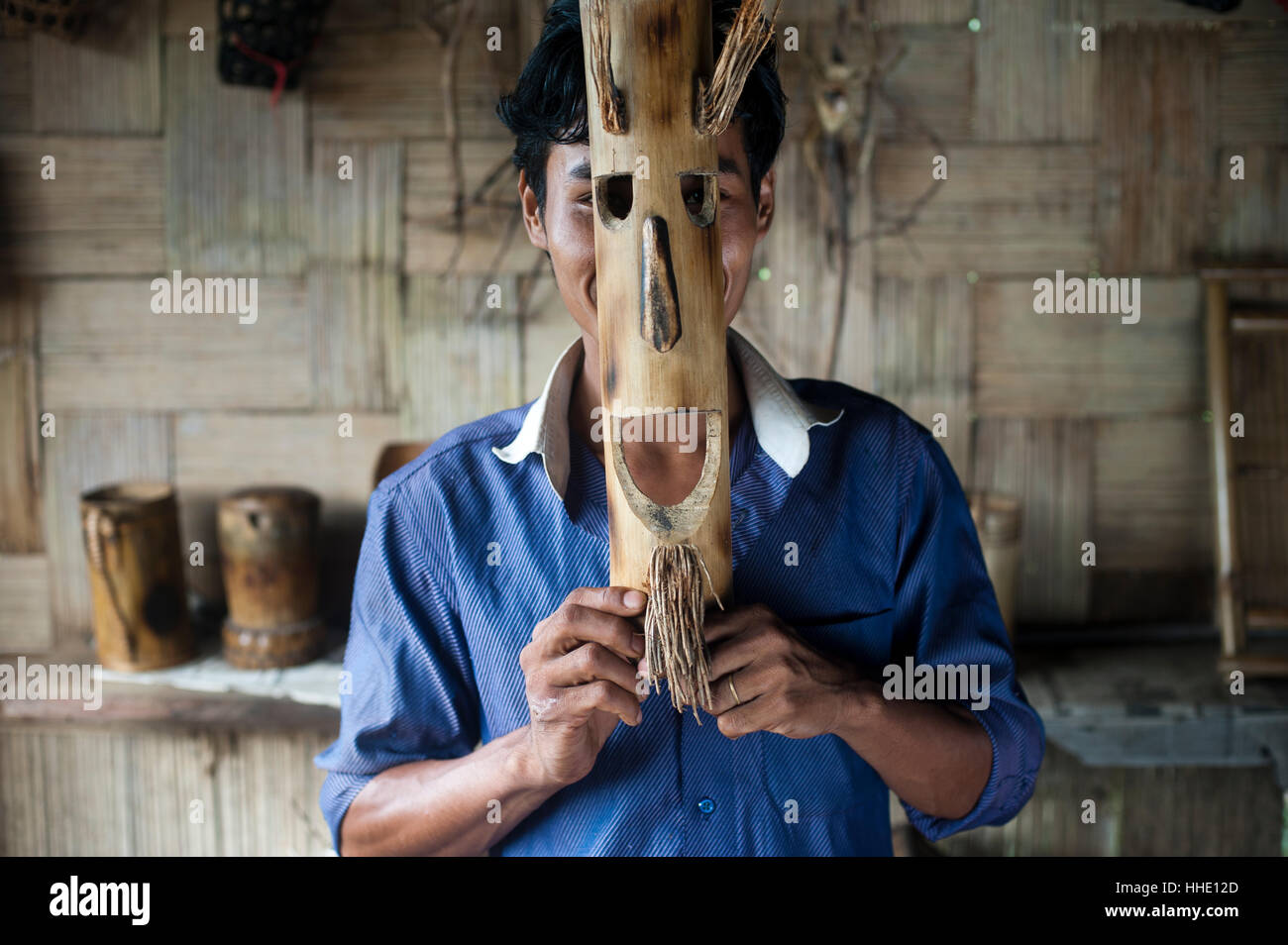 A young man holds a mask made from bamboo to his face, Assam, India Stock Photo