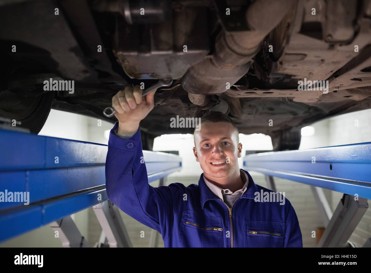 Smiling mechanic looking at camera while repairing a car in a garage ...