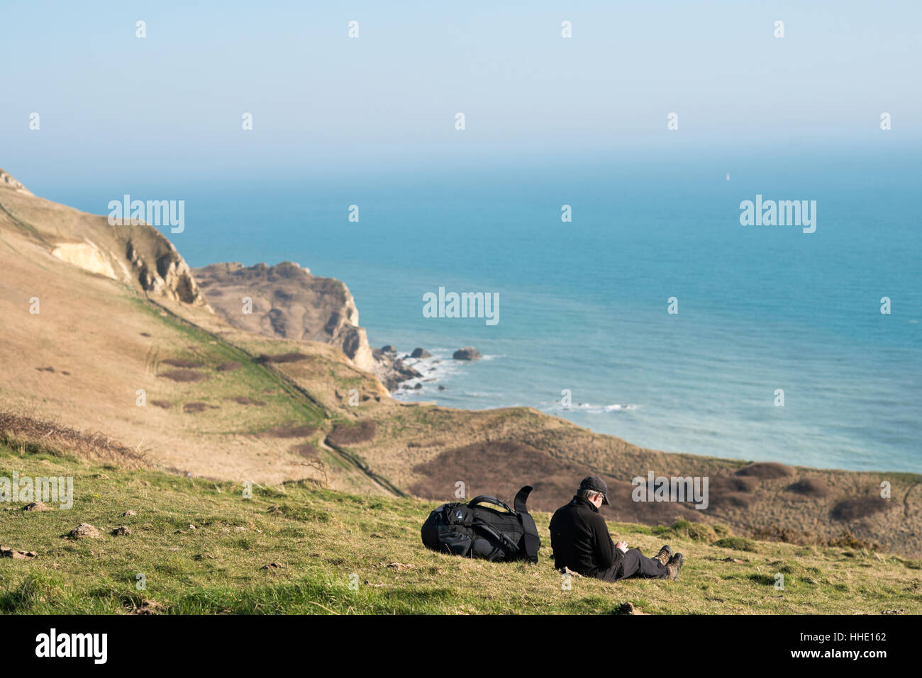 A man takes a break from a coastal walk near Lulworth Cove in Dorset, Jurassic Coast, UNESCO, UK Stock Photo