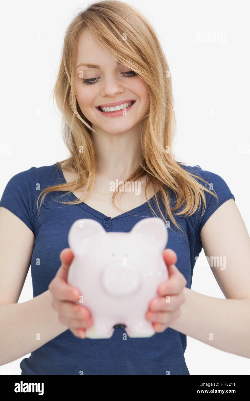 Blonde woman holding a piggy bank while looking it against a white ...