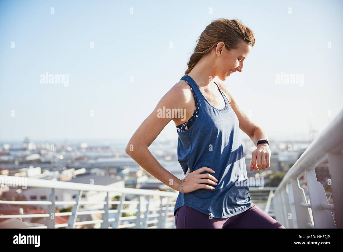 Female runner resting checking smart watch fitness tracker on sunny urban footbridge Stock Photo