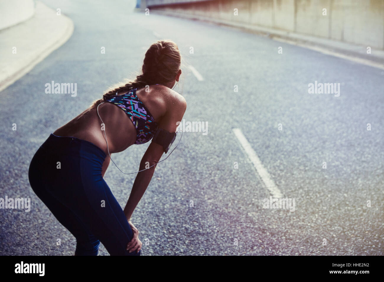 Fit female runner in sports bra with mp3 player arm band resting on urban street Stock Photo