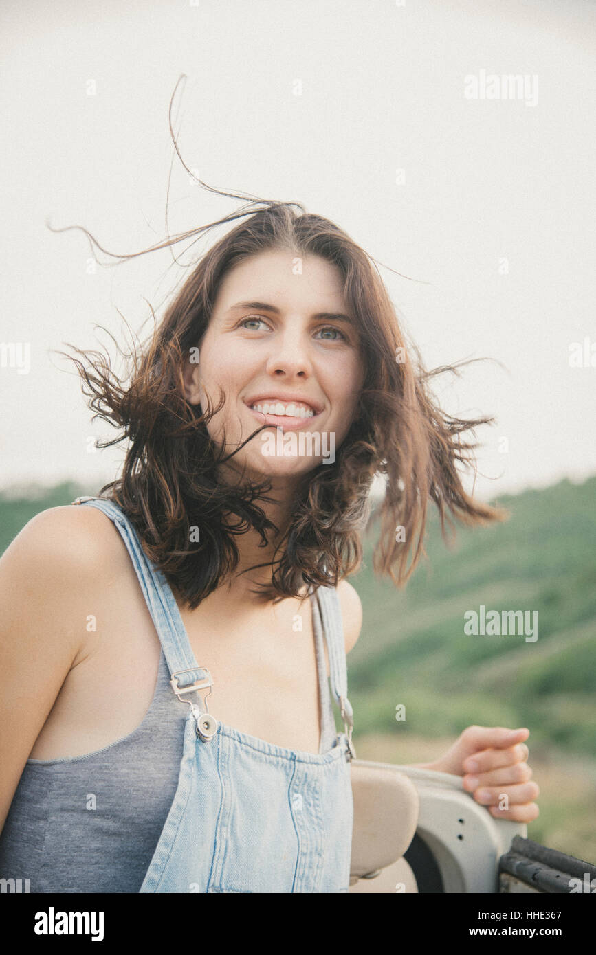 A young woman with windblown hair in dungarees in the mountains. Stock Photo