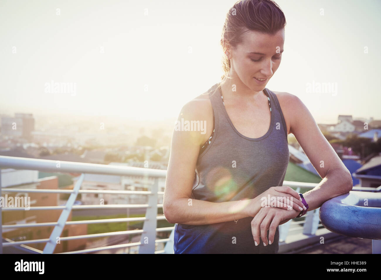 Female runner resting checking smart watch fitness tracker on sunny urban footbridge Stock Photo