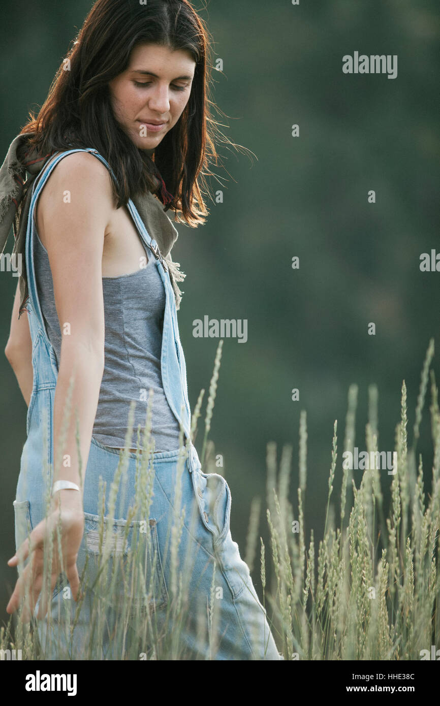 A woman in blue dungarees walking through long grass. Stock Photo