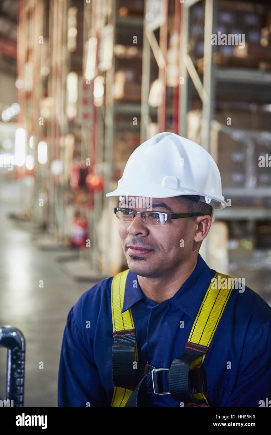 Worker wearing hardhat looking away in distribution warehouse Stock