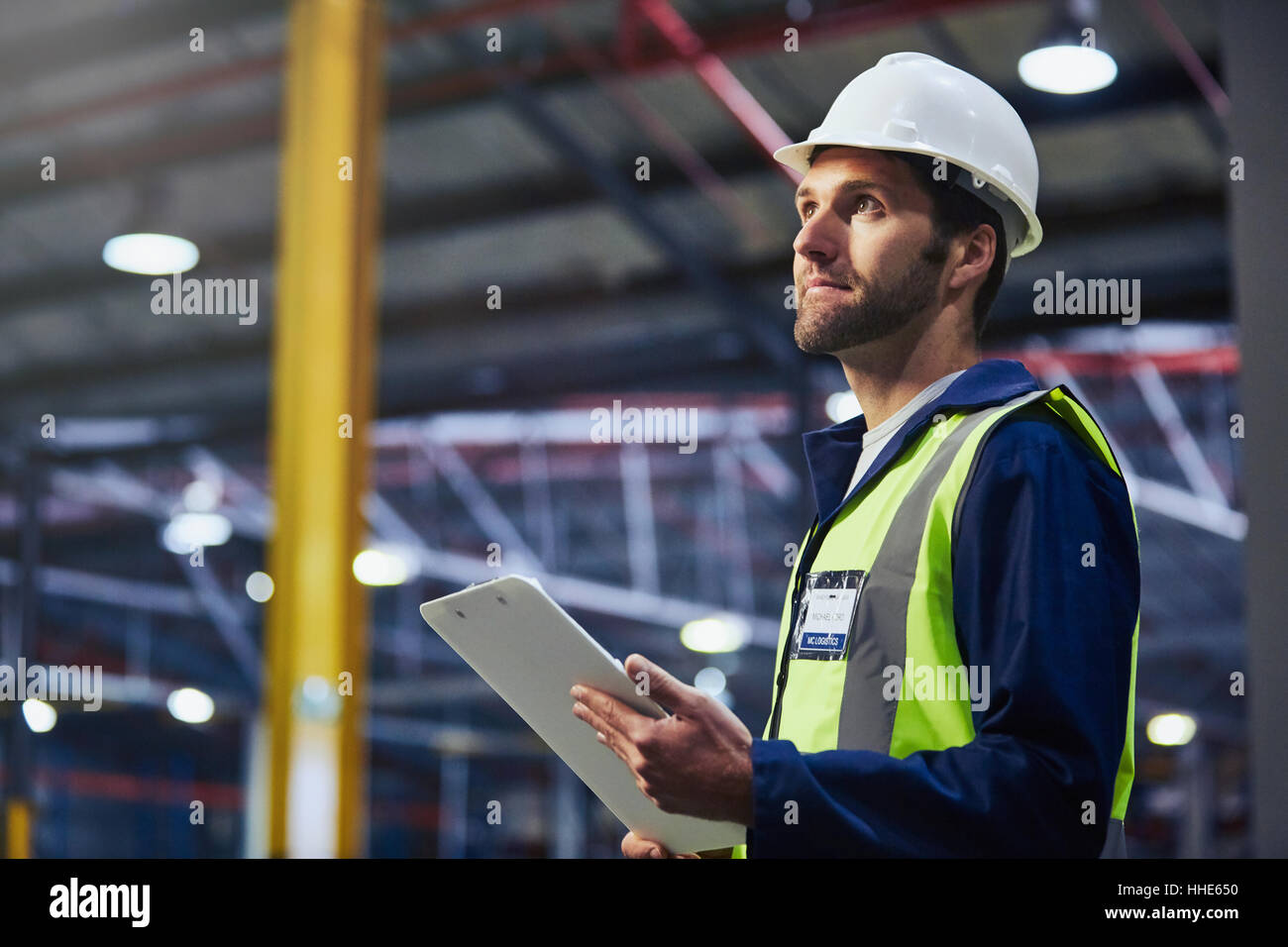 Worker with clipboard looking up in distribution warehouse Stock Photo