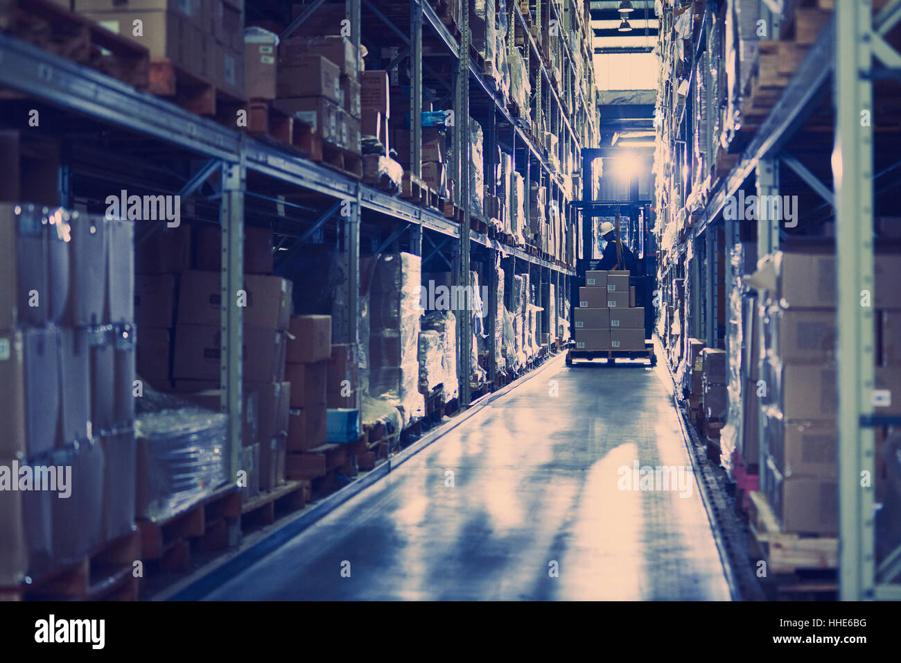 Worker operating forklift moving boxes along distribution warehouse ...
