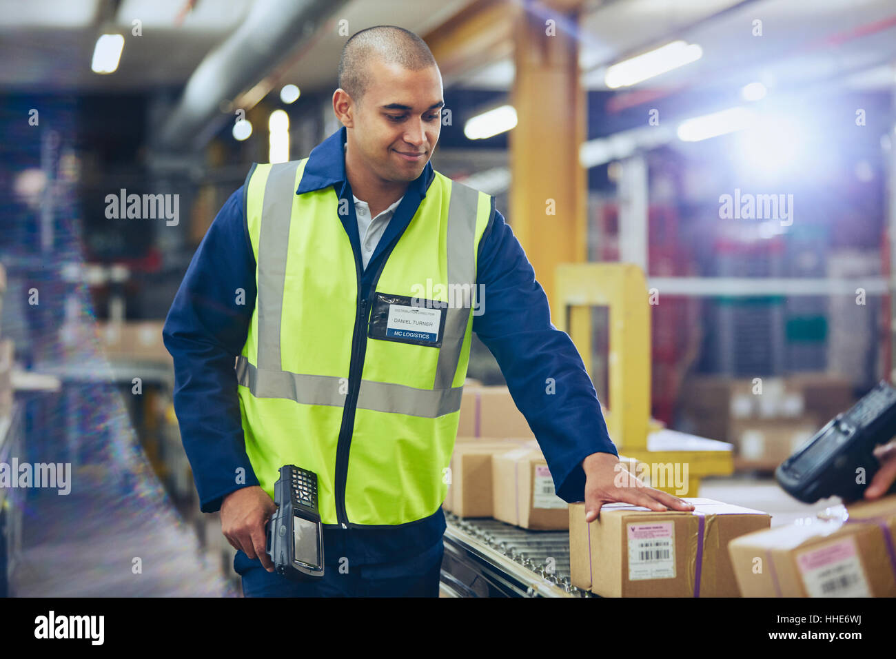 Worker with scanner scanning and processing boxes on conveyor belt in distribution warehouse Stock Photo