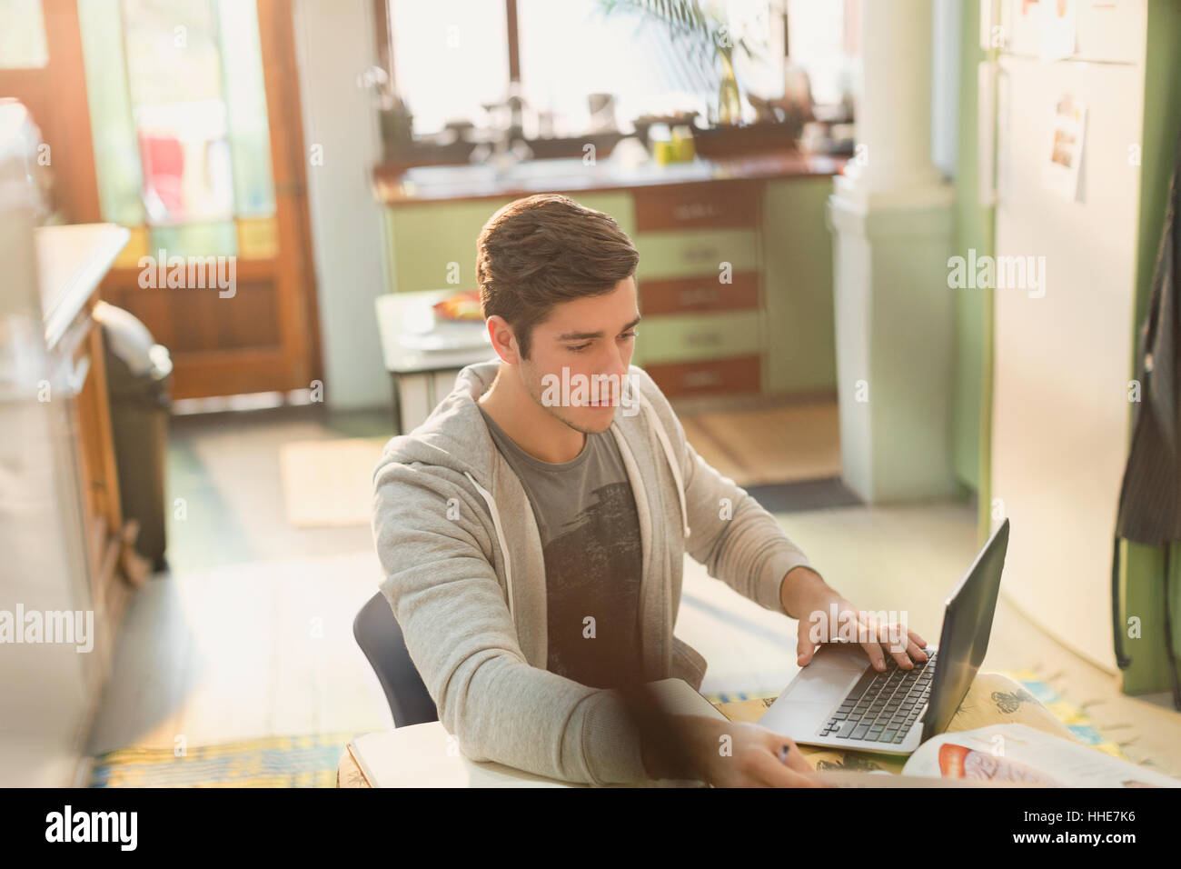 Young man college student studying at laptop in kitchen Stock Photo