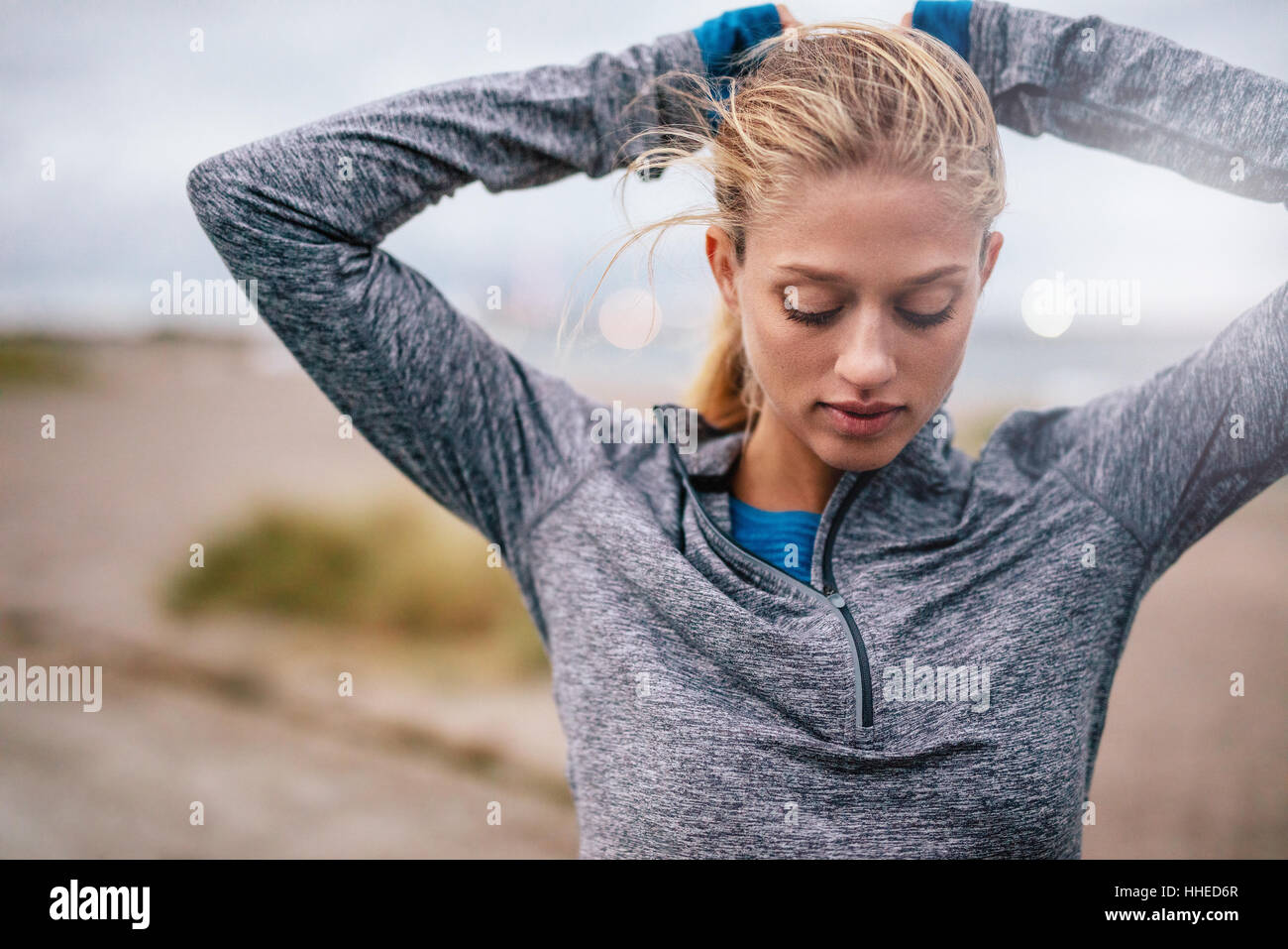 Fit female athlete tying hair before her workout outdoors. Young woman