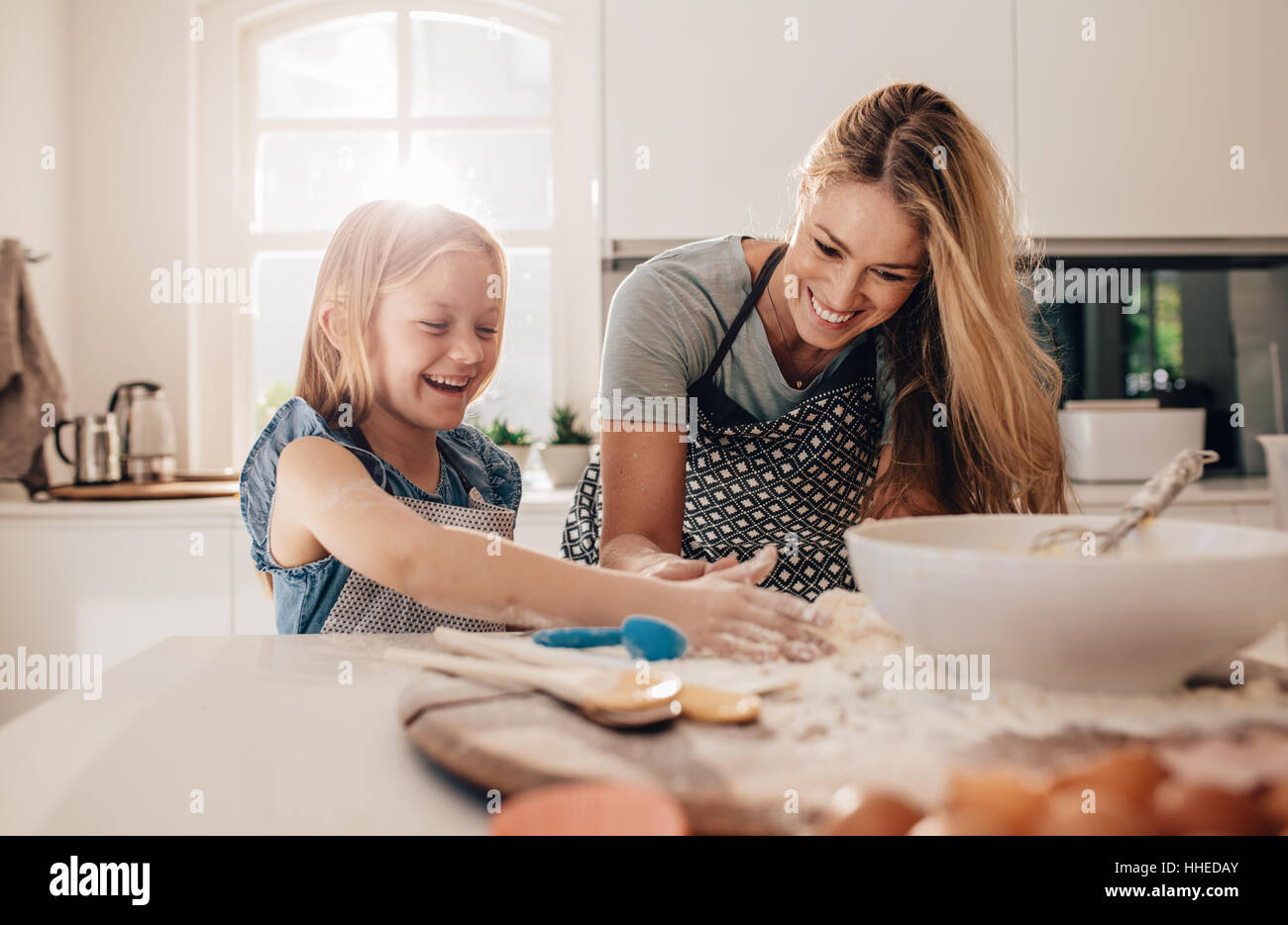 Happy young girl with her mother making dough. Mother and daughter baking in kitchen. Stock Photo
