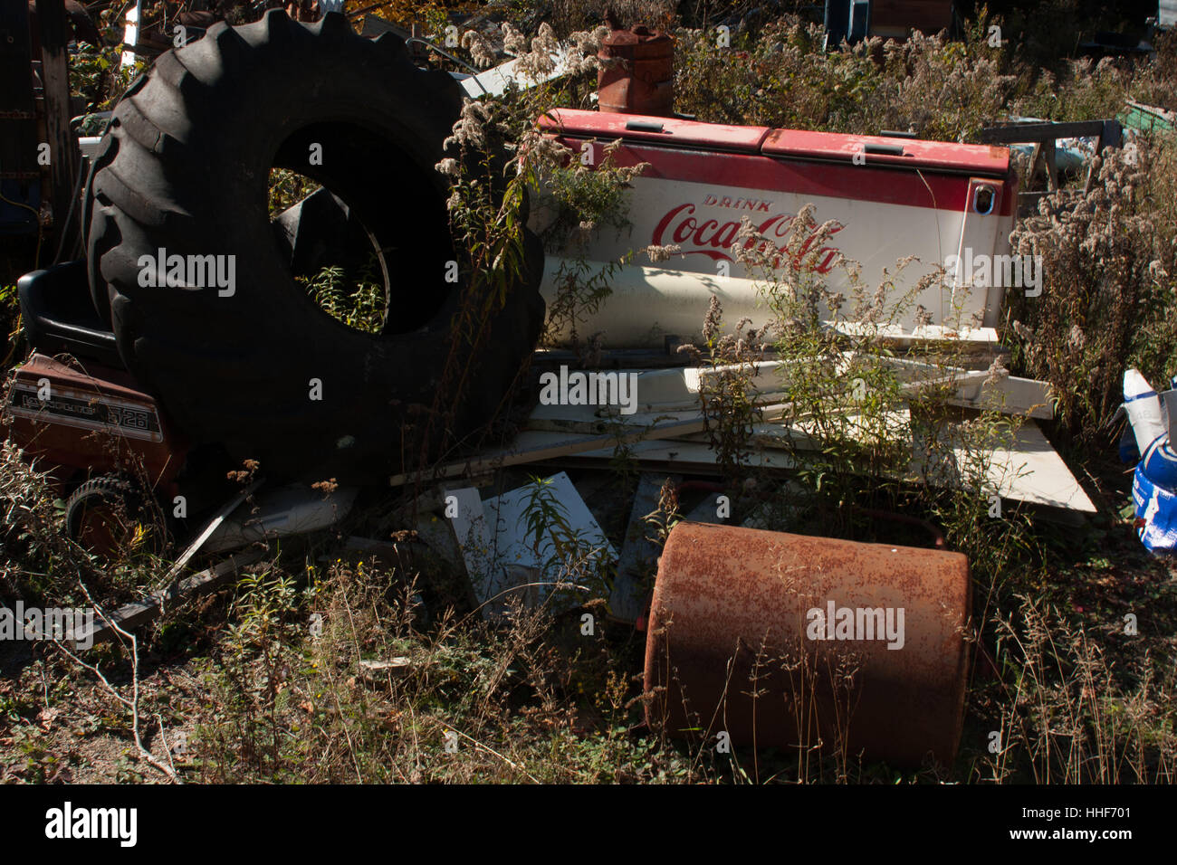 Garbage in a field - an old coca-cola freezer next to a big tractor wheel Stock Photo