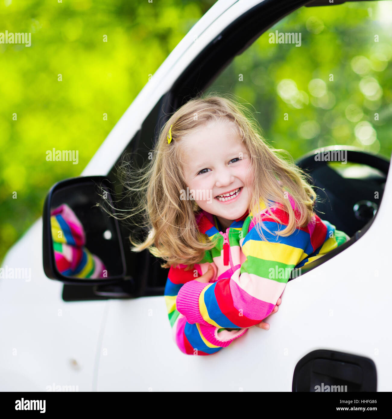Little girl with funny pigtails watching out of car window sitting on front driver seat during a break on a family vacation road Stock Photo