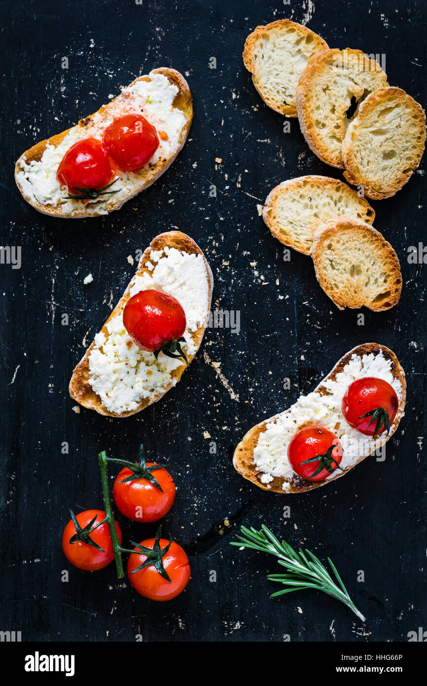 Toast crostini bruschetta with fresh white cheese ricotta, roasted cherry tomatoes and garlic olive oil. Top view Stock Photo