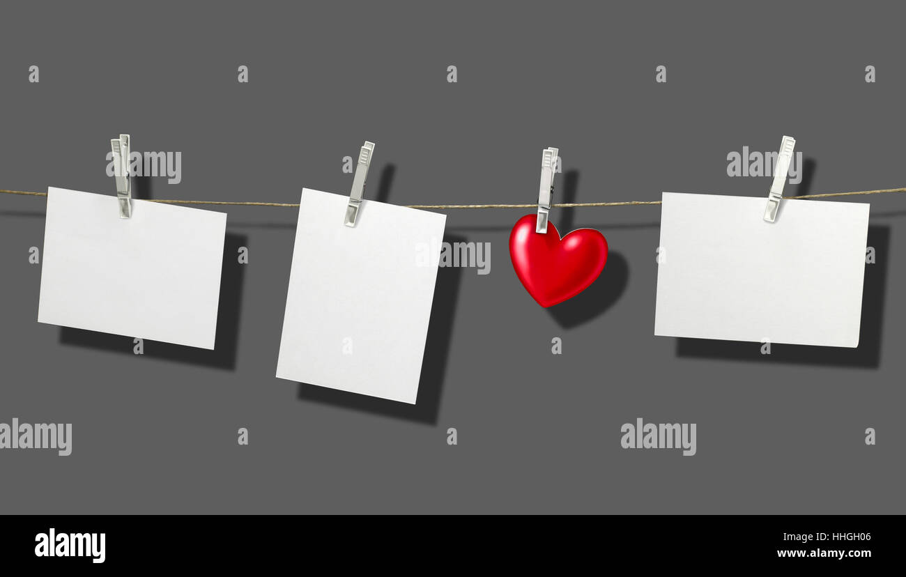 clothesline with some white labels and heart-shape fixed with clothes pins in front of grey back with shadow Stock Photo