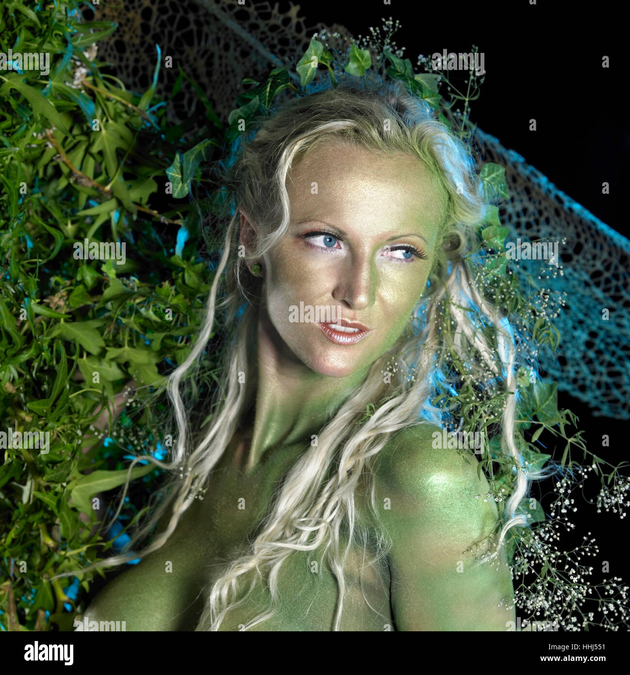 bodypainted woman in front of dark back, partly hidden by green vegetation Stock Photo