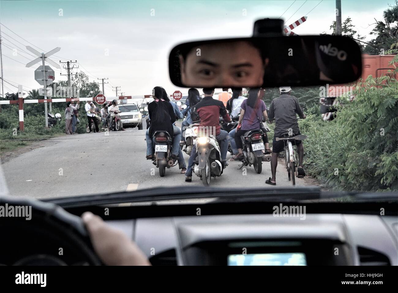 Waiting in the Car at the Level Crossing for the Train to Pass - Drivers Reflection (Eyes) in the Mirror - Cambodia Stock Photo