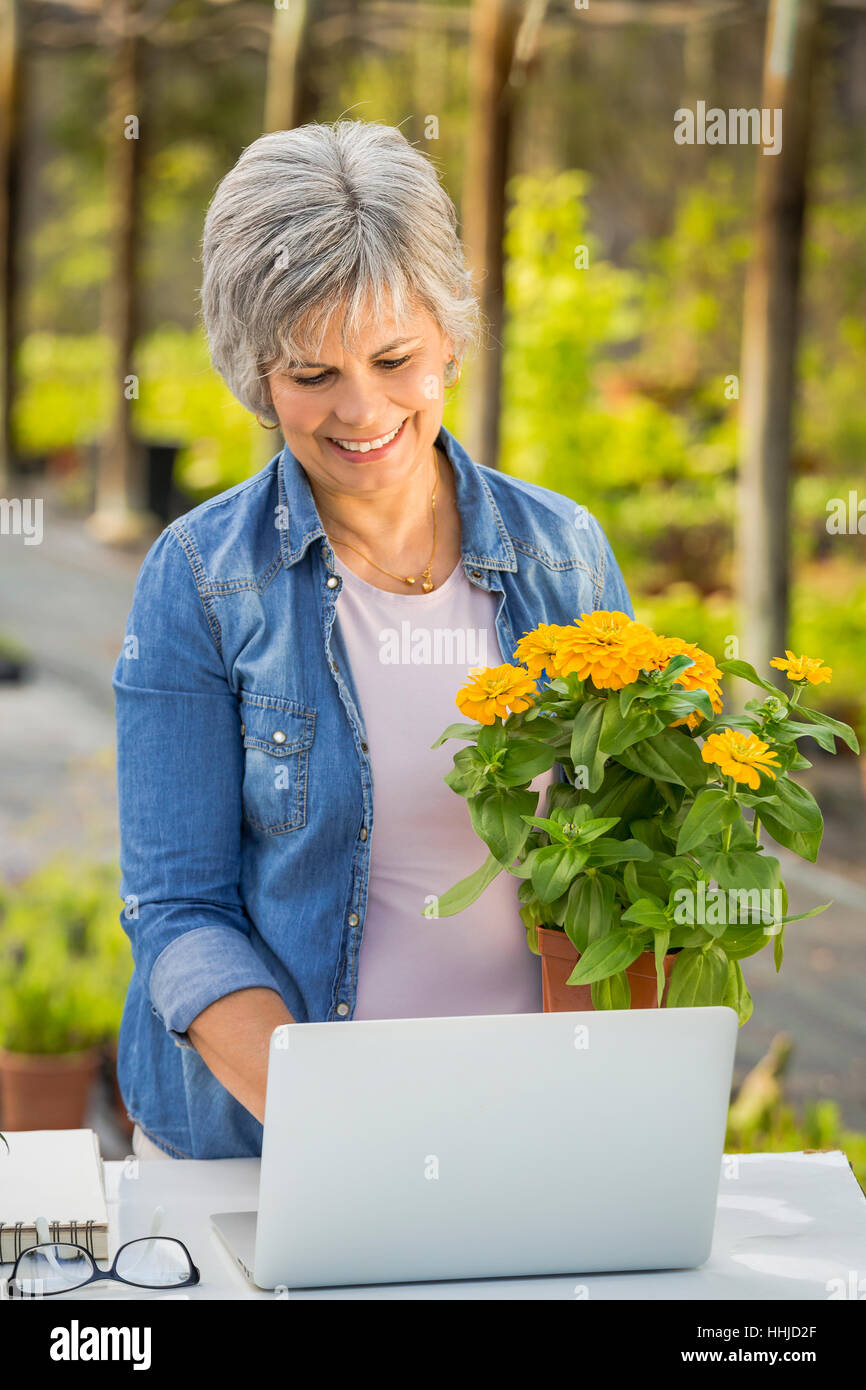 Beautiful mature woman working in a greenhouse holding flowers on her ...