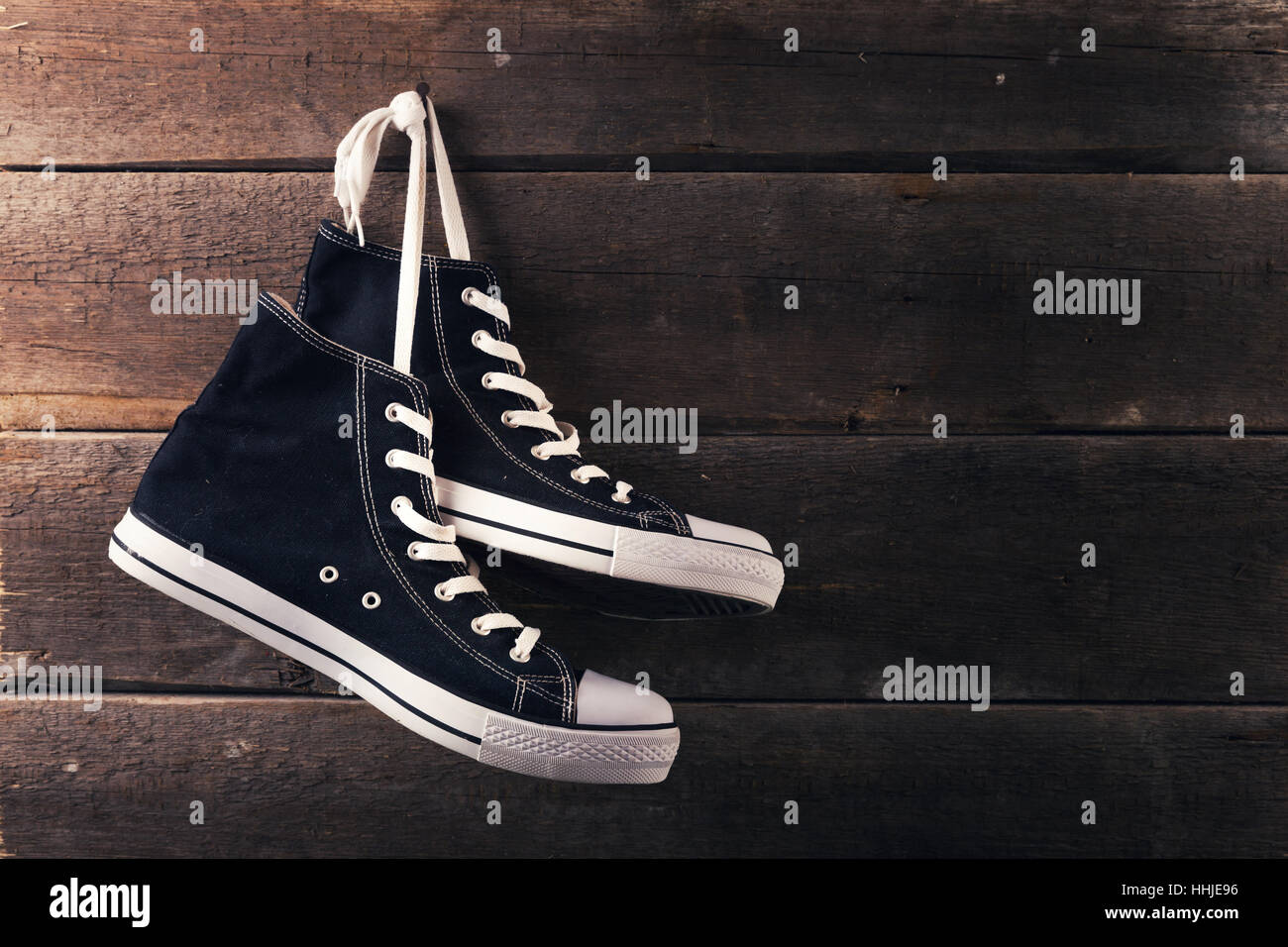 pair of sneakers hang on a nail on a old wooden plank background Stock Photo