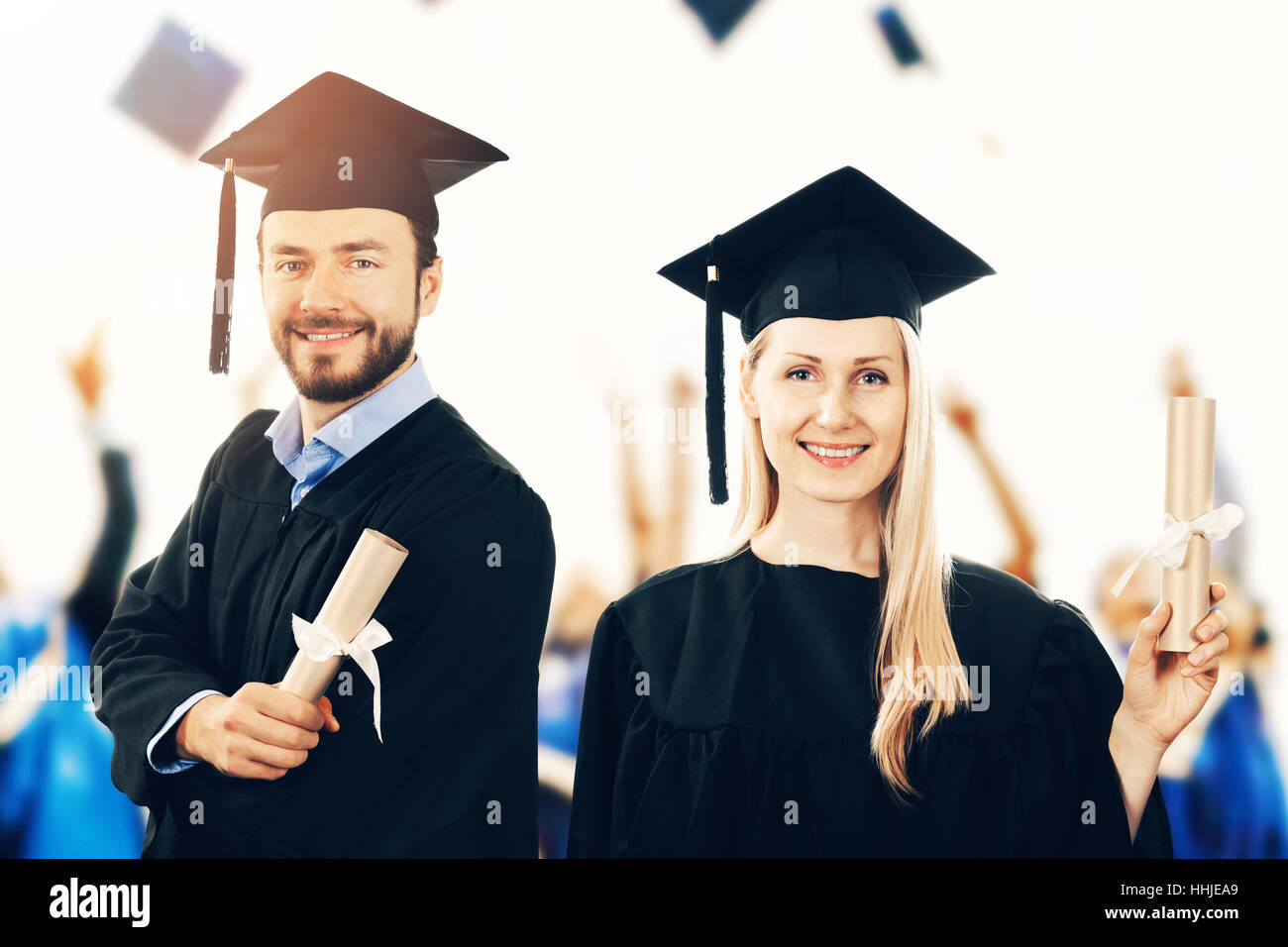 happy graduates with diplomas wearing gowns at graduation ceremony Stock Photo
