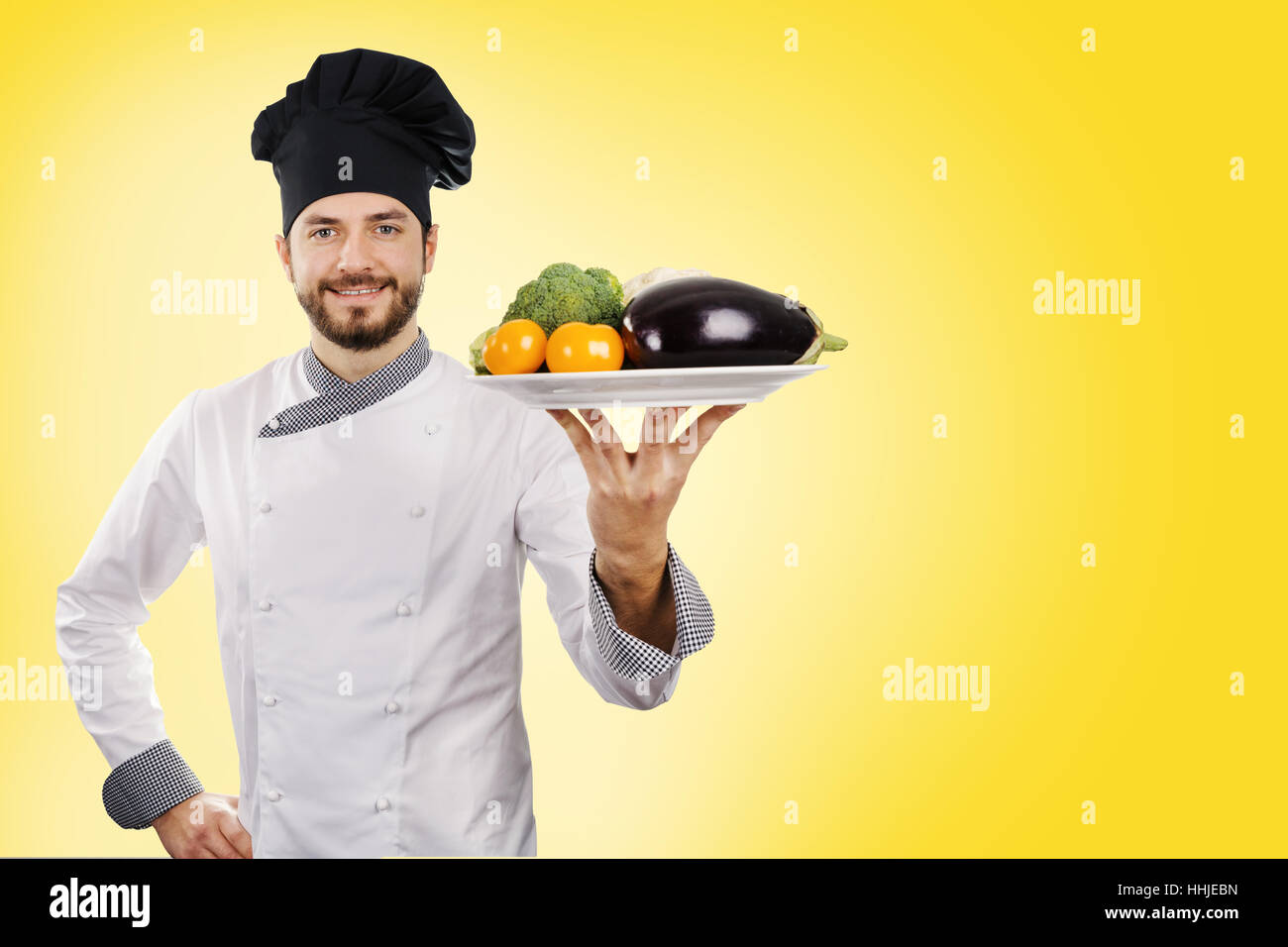 cook holding vegetables plate on yellow background. copy space Stock Photo