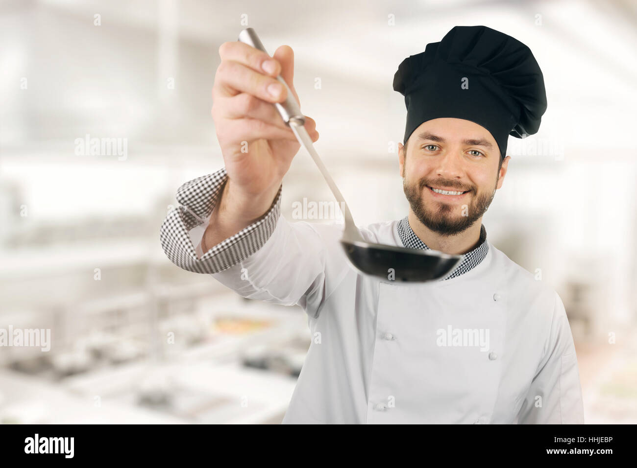 happy chef in restaurant kitchen with ladle in hand Stock Photo