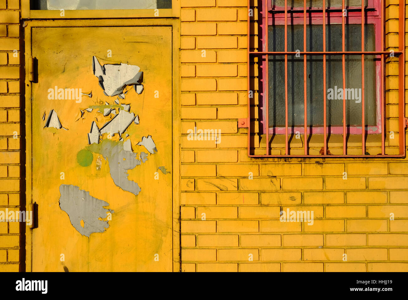 yellow brick wall and door, with iron-barred window Stock Photo