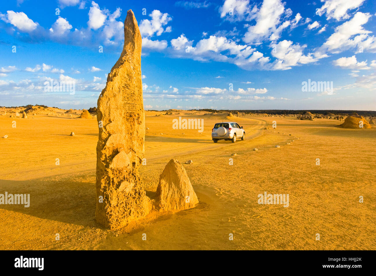 A 4wd driving past one of the limestone pinnacles at the Pinnacles Desert in the Nambung National Park. Western Australia Stock Photo