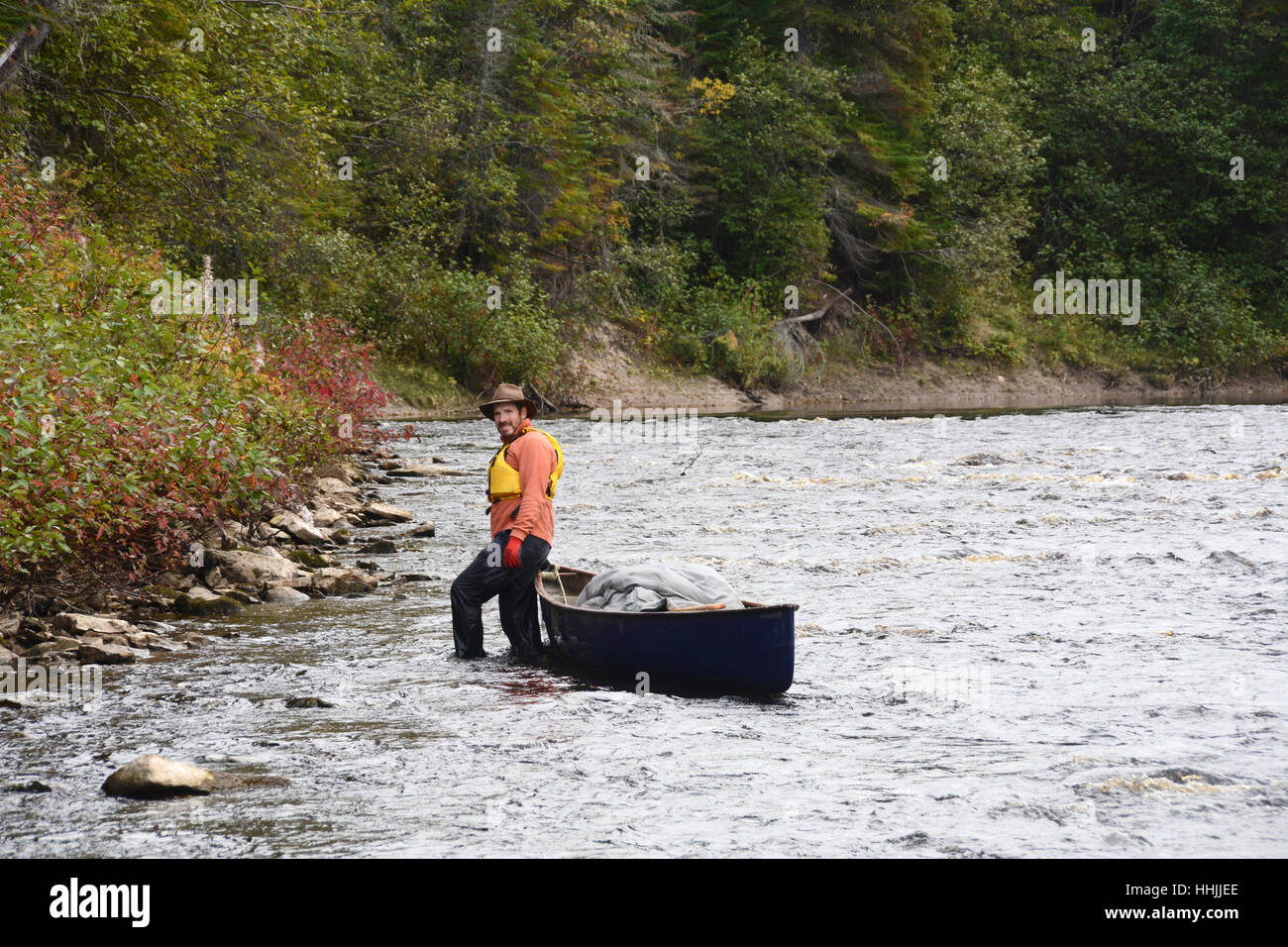 A canoeist pulls his canoe through shallow rapids on the French River in the wilderness of Northern Ontario, Canada. Stock Photo