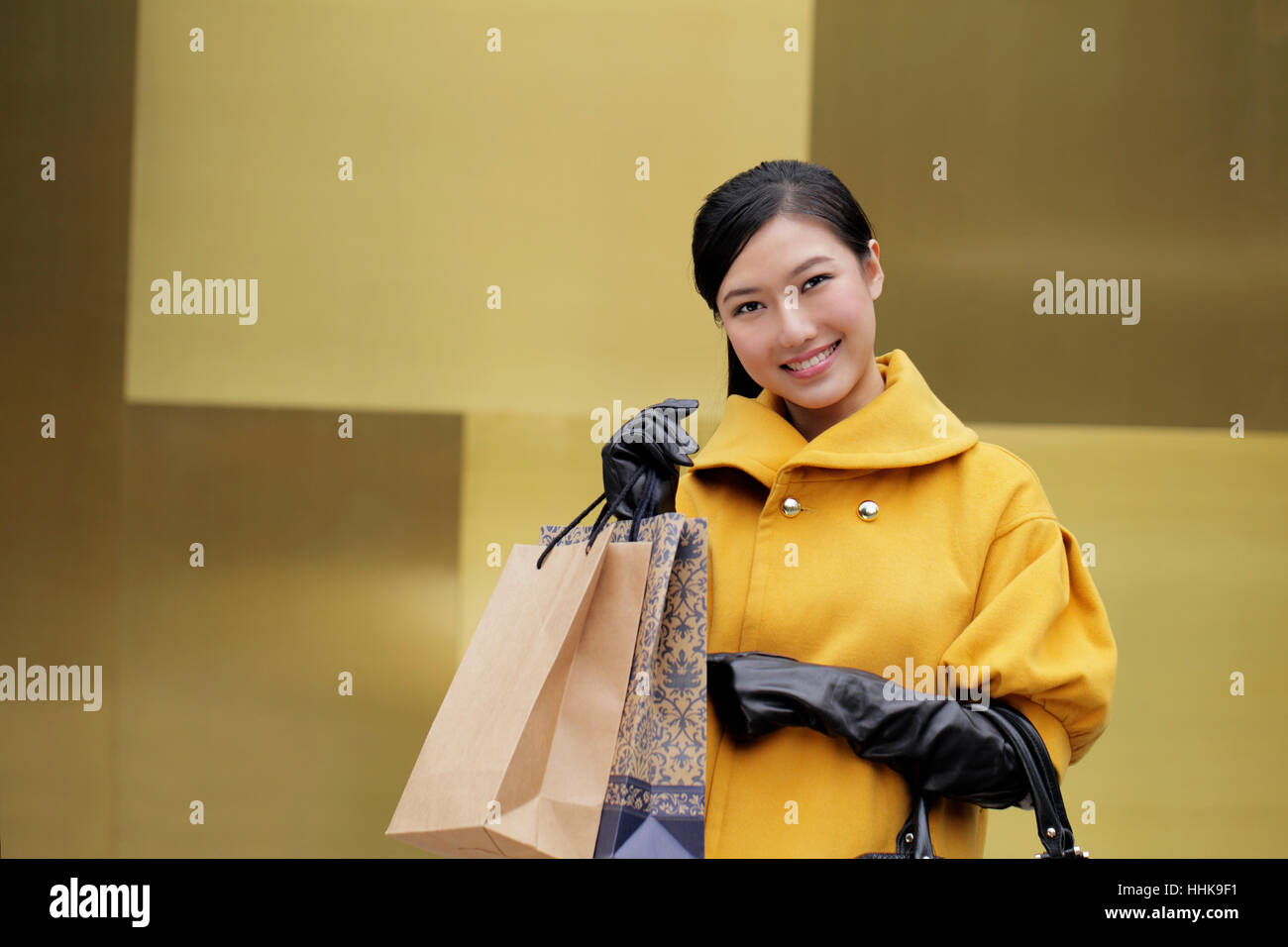 Young woman in yellow coat holding shopping bags Stock Photo - Alamy
