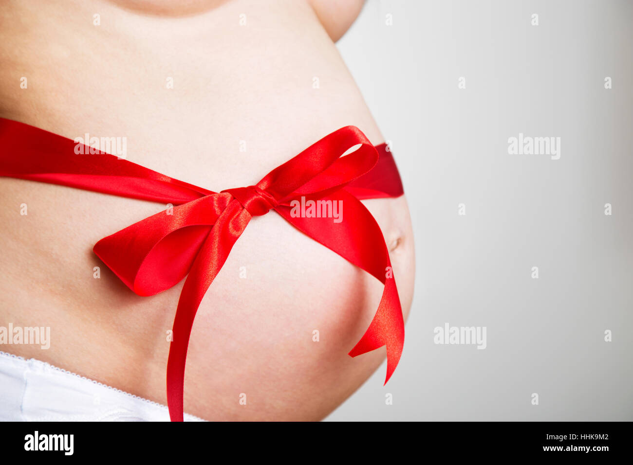 Closeup on belly of expectant pregnant woman with cute red ribbon bow on white background,best present or gift,it's a boy, young family, new life conc Stock Photo