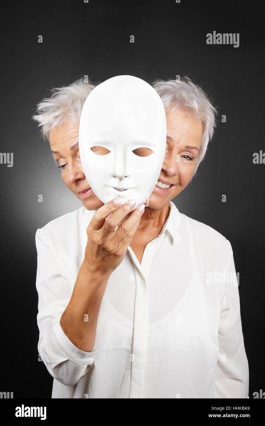 older woman hiding happy and sad face behind mask Stock Photo