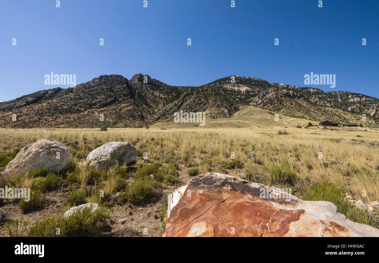 The arid landscape of the prairie in late summer with view of foothills of Rocky Mountains and isolated ranch house in summer. Stock Photo