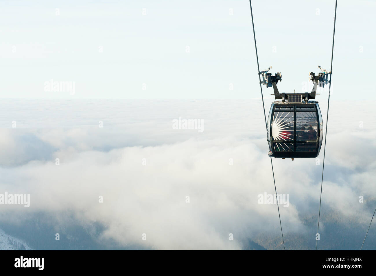 Cable car cabin going up above the clouds to the top of a mountain at a ...