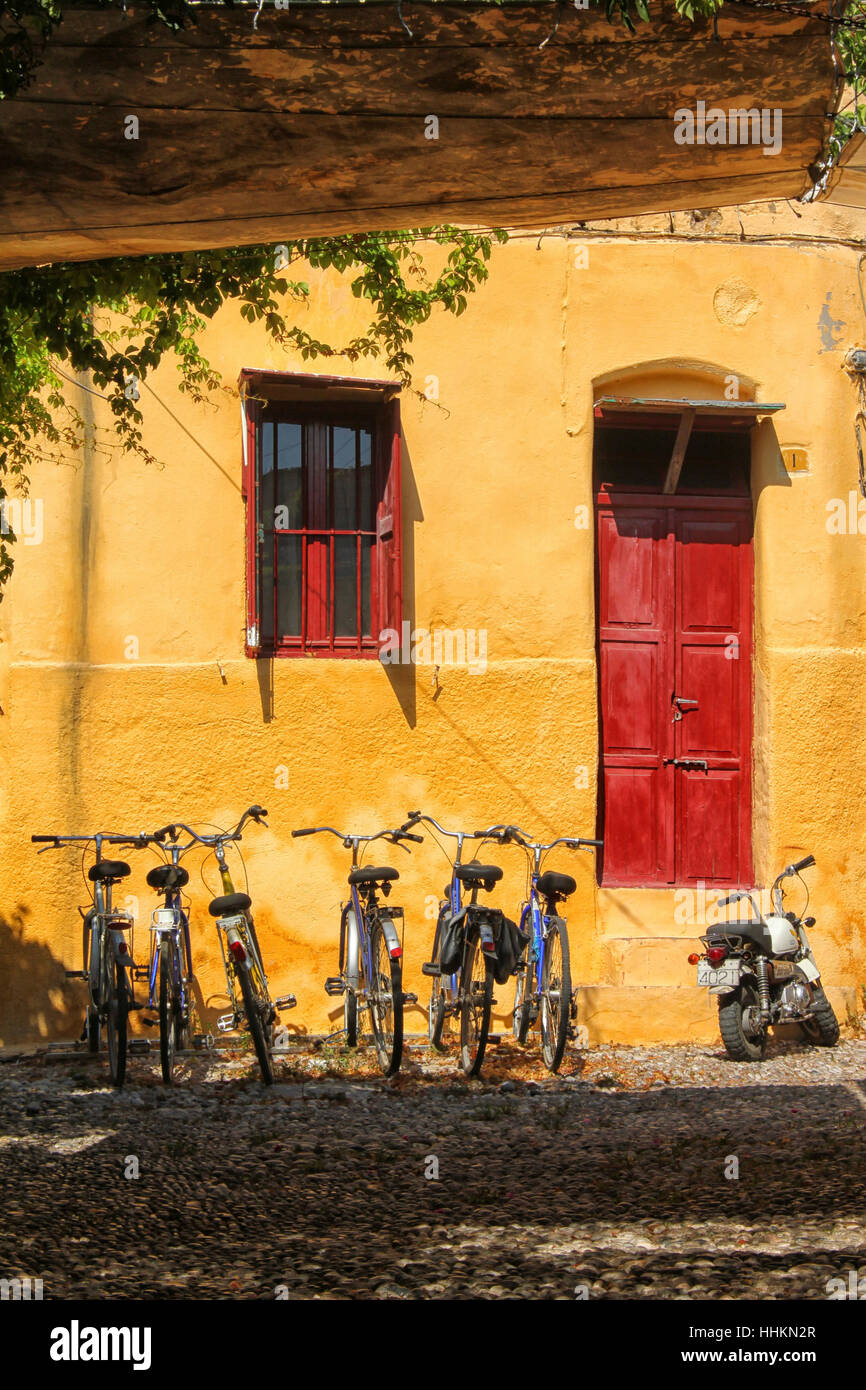 Bicycles against a yellow wall with a red door and red window in Rhodes, Greece Stock Photo
