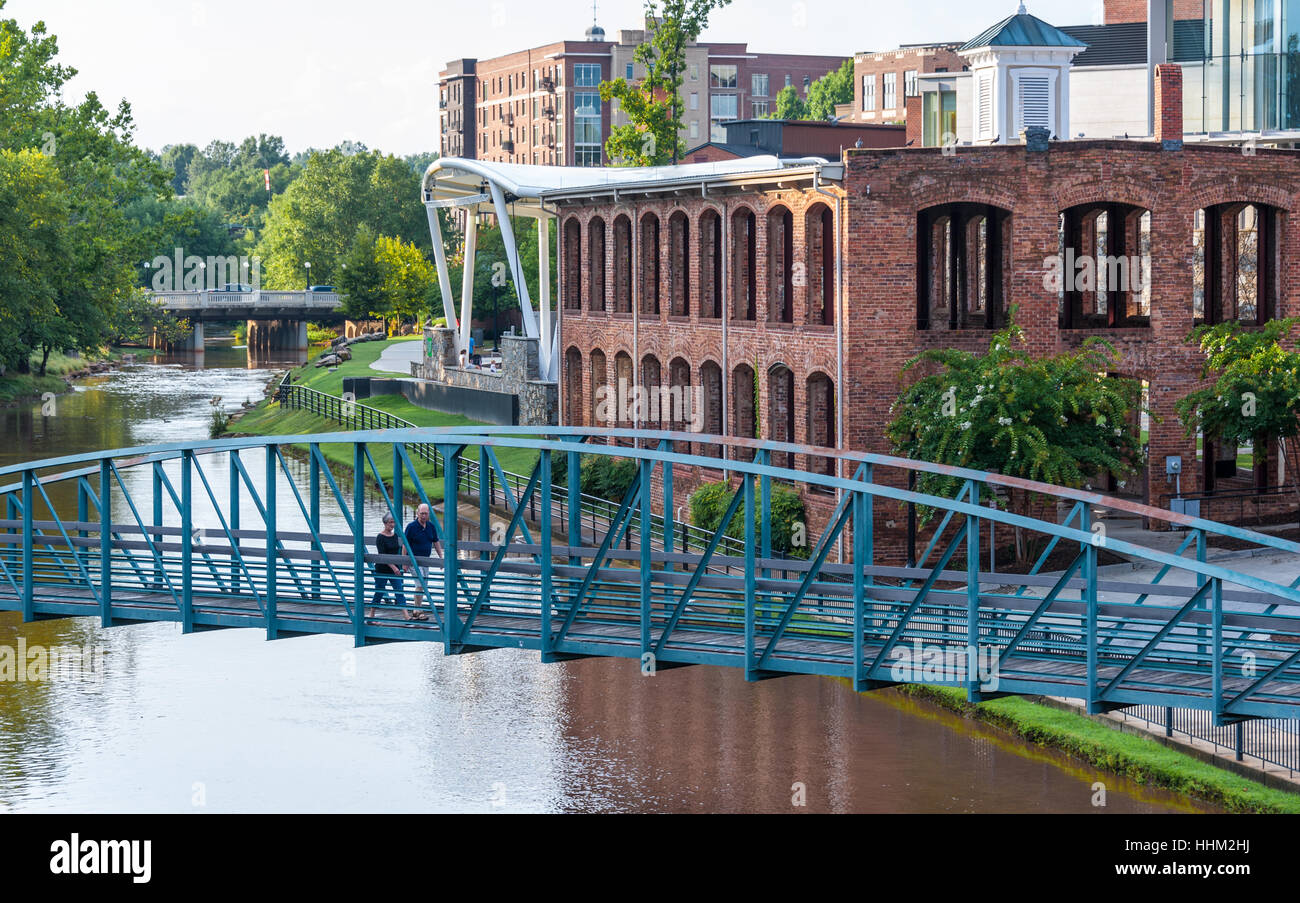 Couple crossing a pedestrian footbridge over the Reedy River along Main Street in historic downtown Greenville, South Carolina. Stock Photo