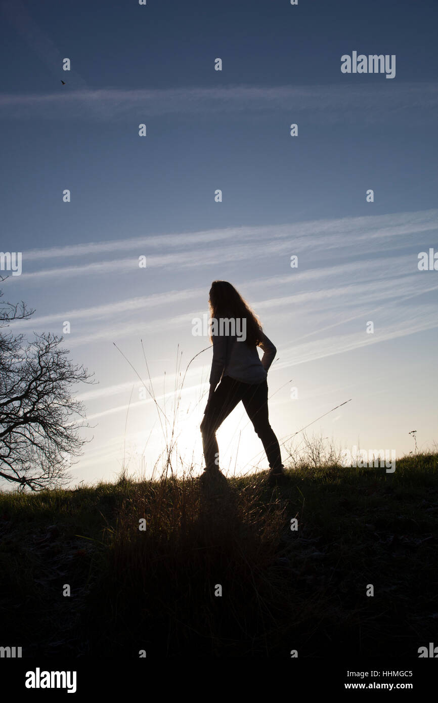 Silhouette of an unrecognisable woman standing alone sunset sky. Stock Photo