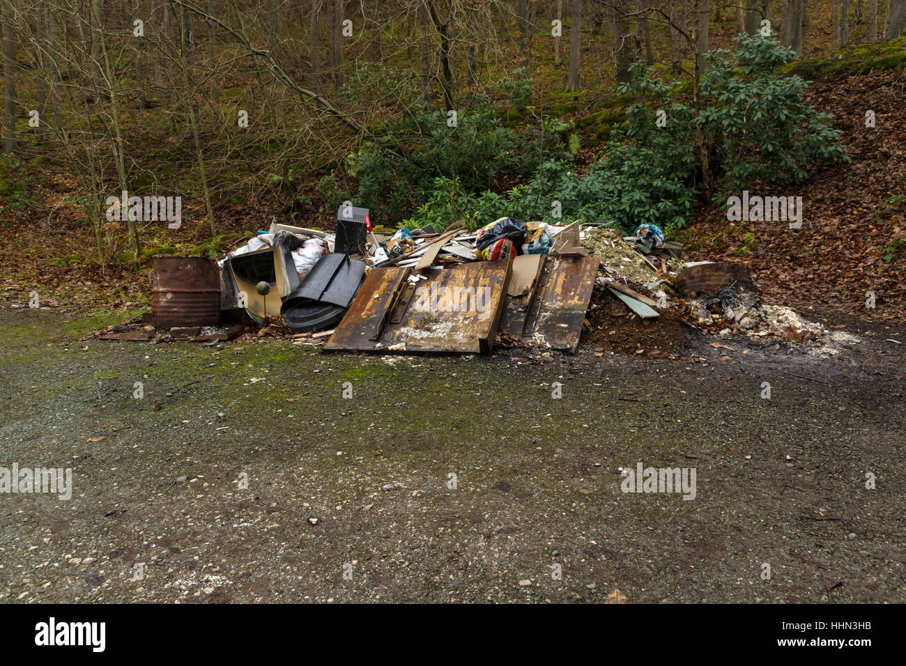 Dumped rubbish and garbage in a forest an example of fly tipping or illegal dumping on a forest trail in North Wales Stock Photo