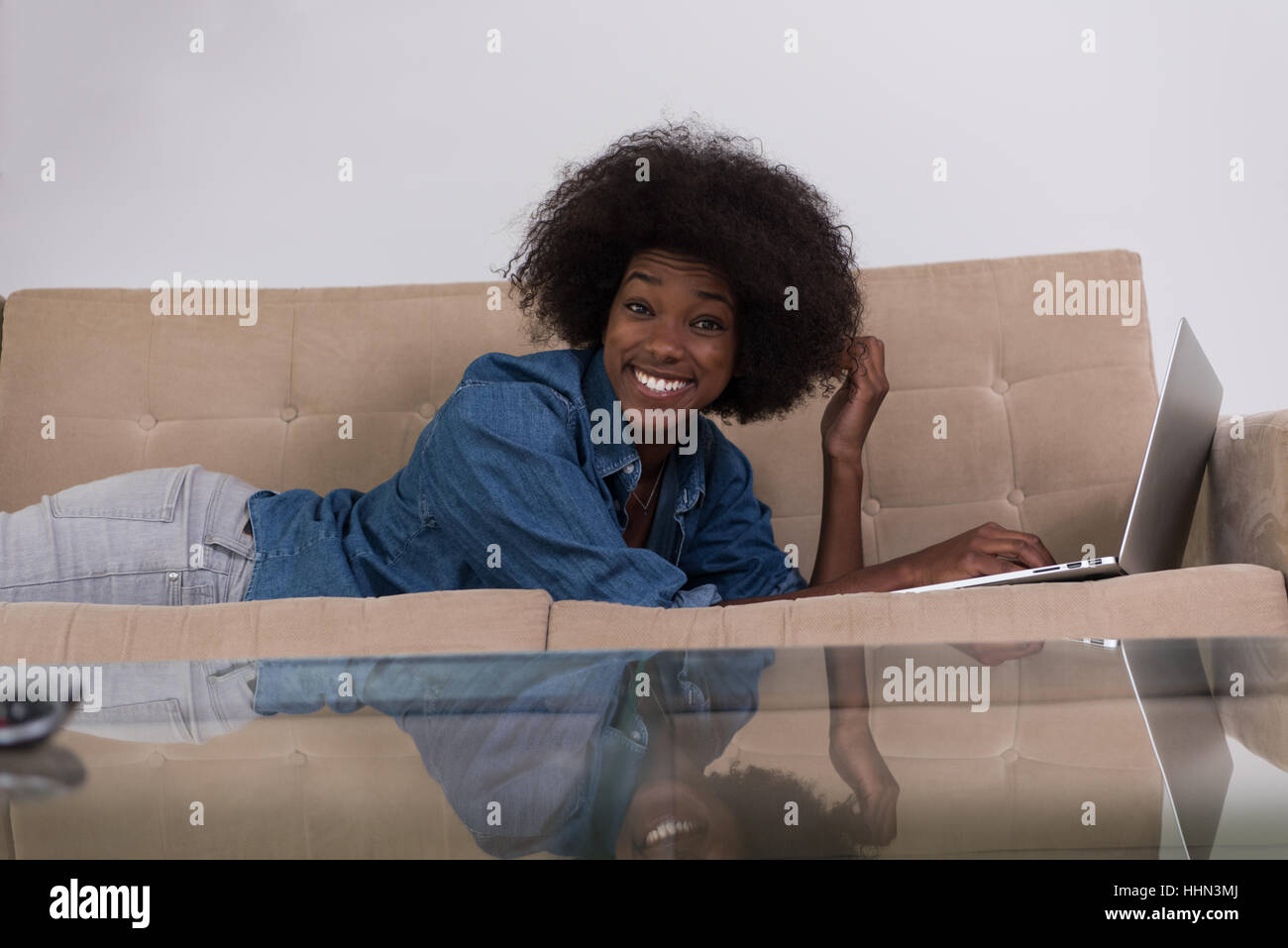 Smiling young African American woman using laptop while relaxing on ...