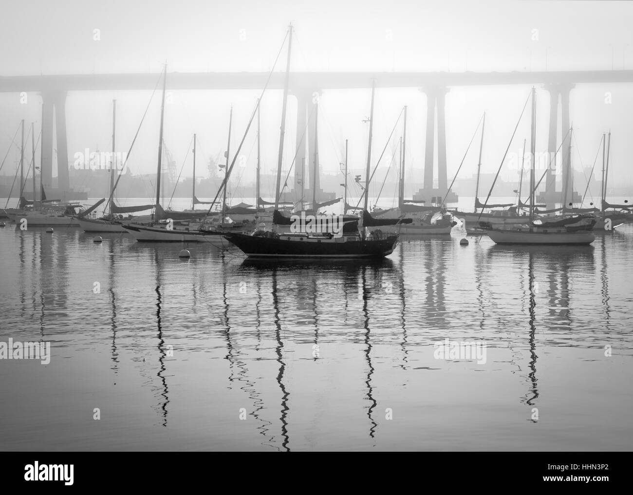 Sailboats anchored off the coast of a foggy Tidelands Park in Coronado, CA with the US Navy fleet in the background. Stock Photo