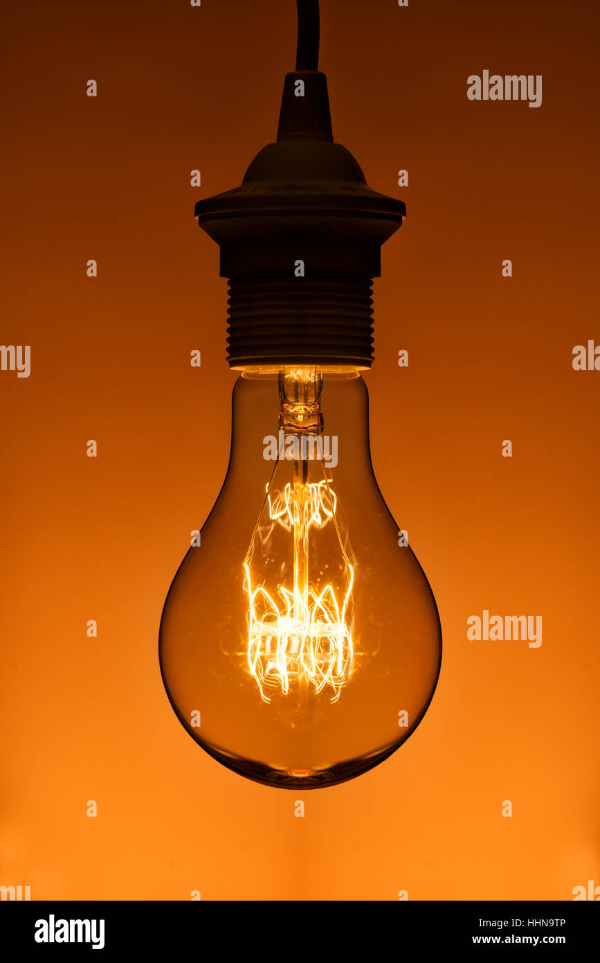 lighted vintage incandescent bulb on orange background Stock Photo