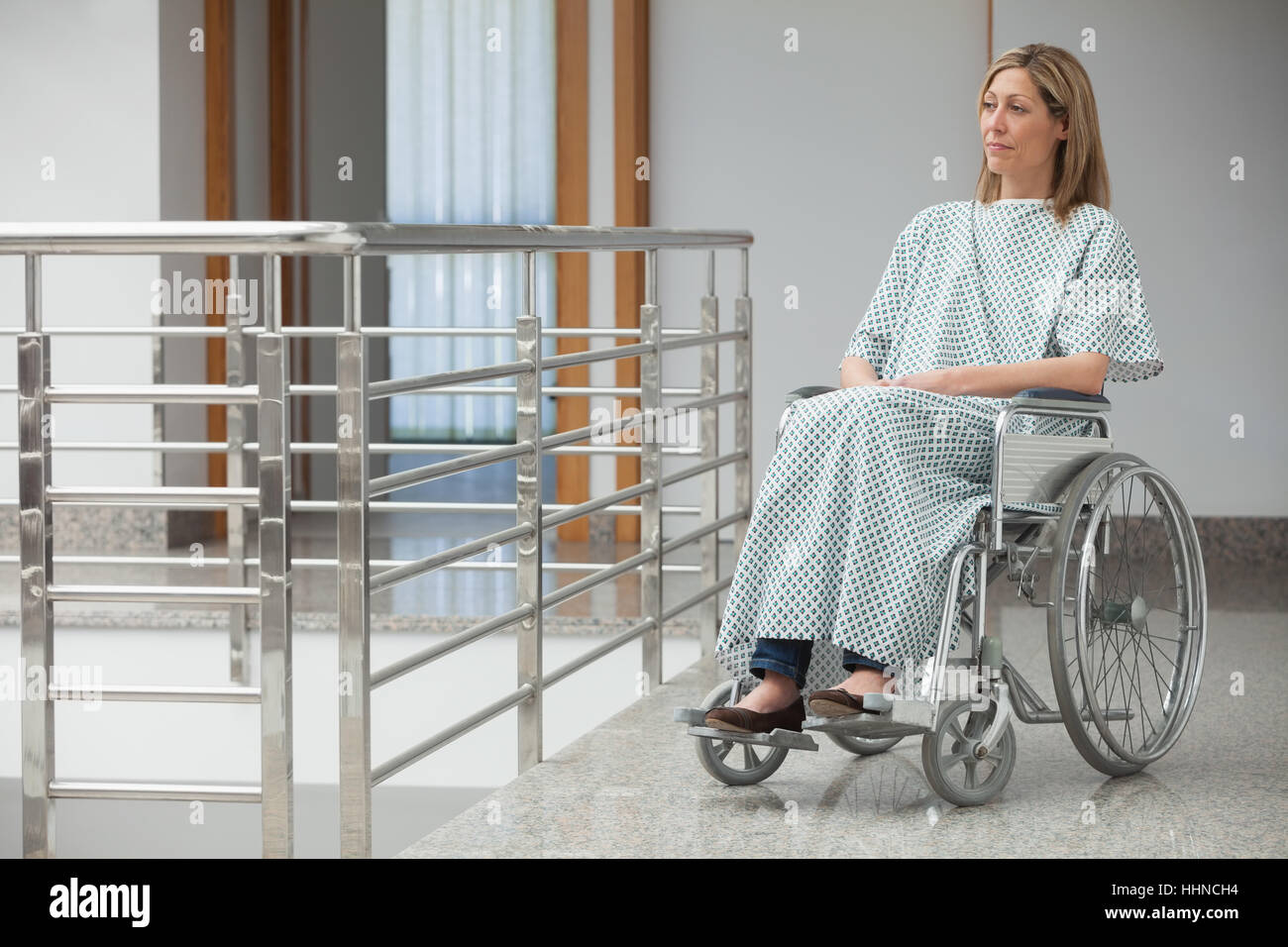Woman wearing hospital gown and sitting in wheelchair in hospital