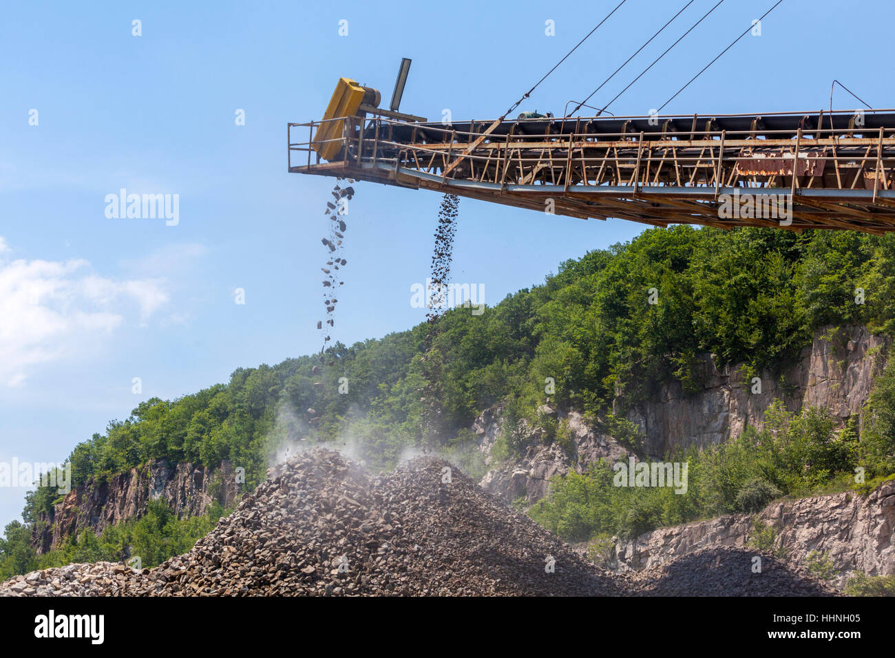 A conveyor belt transports crushed rock in a rock quarry into large mounds. Stock Photo